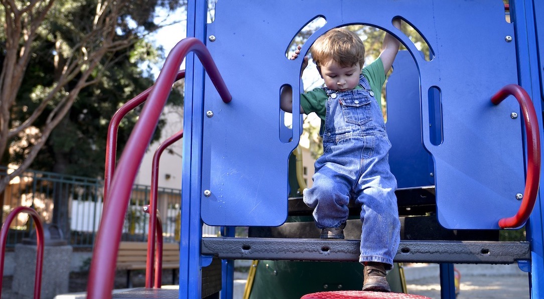 Young boy stepping down from tall blue playground equipment platform onto a red step