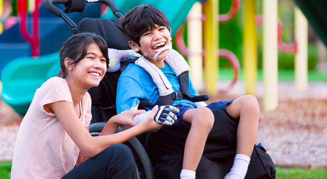 Sister sitting next to disabled brother in wheelchair at playground